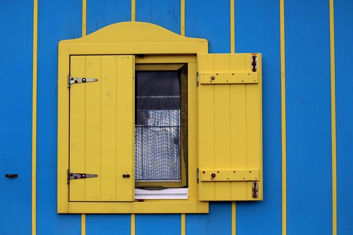 Fenêtre jaune avec un volet ouvert sur un mur bleu strié