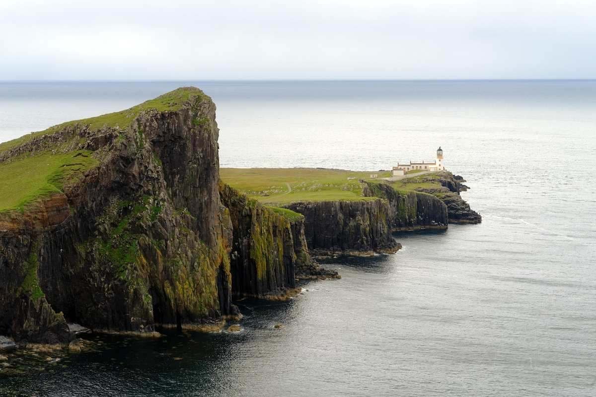 Falaises abruptes couvertes d'herbe, phare au bout, mer calme Falaises abruptes couvertes d'herbe, phare au bout, mer calme
