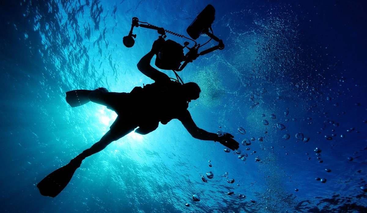 Un plongeur en silhouette filme sous l'eau avec un appareil