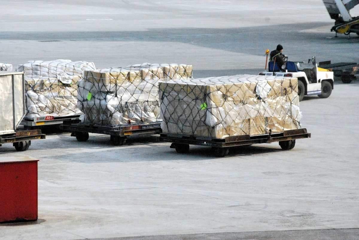 Colis emballés sur des palettes à l'aéroport, un véhicule de service visible