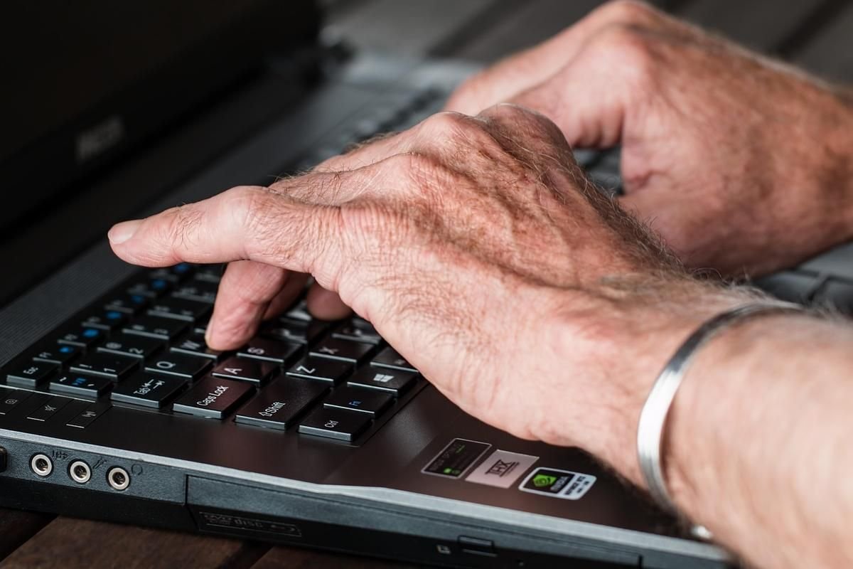Des mains ridées tapent sur le clavier d'un ordinateur portable